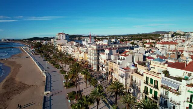 Drone flight back over in along coast beautiful beaches surrounded by Palm trees in Sitges. Mediterranean landscape of beach and hotels. Gentle sea waves quietly roll onto shore. Film intro. 4K video