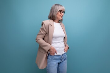 a mature woman with gray hair in a jacket stands confidently against a bright background with copy space