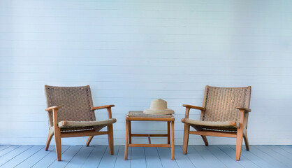 Set of two wicker chairs and table with straw hat on the table, rattan armchairs set, white wooden...