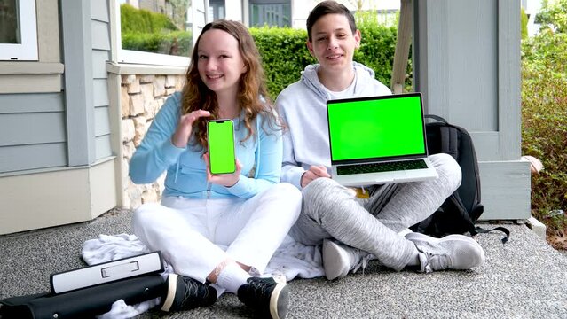 teen boy and teenage girl sitting outdoors with folders backpack holding laptop and phone green screen chroma key ad look here school presentation on computer. kid ready for video lesson
