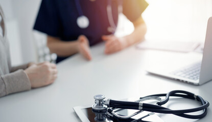 Stethoscope lying on the tablet computer in front of a doctor and patient at the background. Medicine, healthcare concept