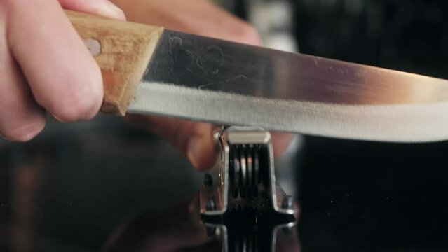 Man Sharpening the knife with a whetstone on a wooden background close up.