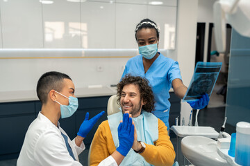 Obraz na płótnie Canvas Satisfied male patient and confident female dentist specialist giving each other high five after successful finished dental treatment during appointment at modern dentist's office.