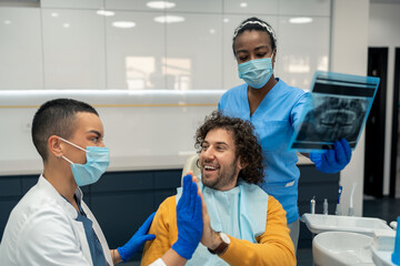 Happy satisfied male patient and female dentist specialist giving each other high five after...