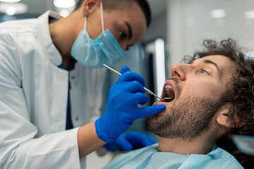 Young man with mouth open having dental exam during appointment at dentist's office, getting his...