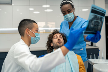 Dental assistant showing dental x-ray orthopantomogram of patient's jaws to dental specialist orthodontist and patient who is feeling scared and uncomfortable at dentist's office.