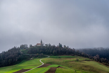 Fototapeta na wymiar Morning fog is lifting from behind a hill with a church south east part of Slovenia