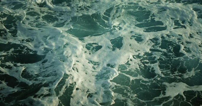 Boiling ocean waves foam water background at storm. Top down raging sea surface close-up slow-motion.