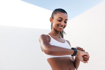 Smiling woman checking heart rate on smartwatch after outdoors exercising. Young female in fitness attire looking at fitness tracker.