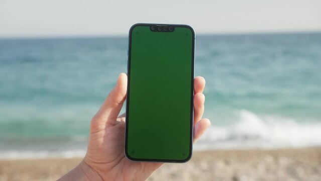 Green Screen chroma key Handheld Smartphone. Travel with phone concept, application mock up. Sunset on a tropical beach.