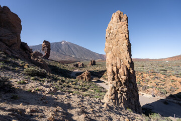 un rocher en forme de menhir , debout devant un paysage avec un chemin qui mène vers un volcan en arrière plan
