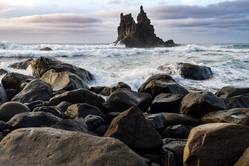 une plage avec de gros rochers et un îlot pointu et inquiètant en arrière plan 