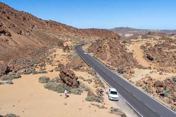 Une voiture garsée au bord d'une route qui traverse un désert de roche ocres