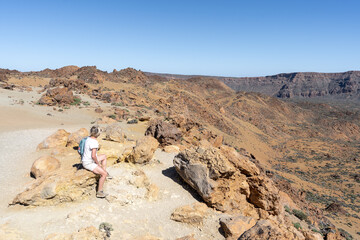 une personne assise sur un rocher face à un décors martien, volcanique et désertique