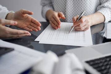 Fototapeta premium Woman accountant using a calculator and laptop computer while counting and discussing taxes with a client. Business audit and finance concepts