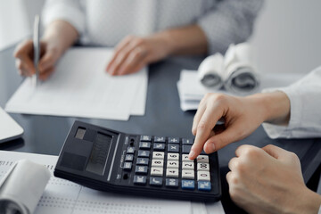 Woman accountant using a calculator and laptop computer while counting taxes for a client. Business...