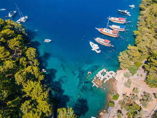 Aerial view of tour boats and private yachts and swimmers enjoying the beautiful Kleopatra Hamamı Cove, located between Göcek and Dalaman, Turkey, known for its crystal-clear waters and ancient ruins.