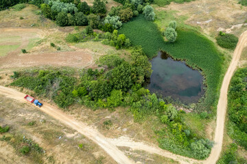 A view from above of a lake between green trees and bushes. A dirt road passing by a lake.