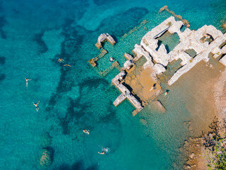Aerial drone photo of swimmers enjoying the beautiful Kleopatra Hamamı Cove, located between G&ouml;cek and Dalaman, Turkey, known for its crystal-clear waters and ancient ruins.