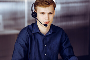 Young blond businessman using headset and computer at work. Startup business means working hard and out of time for success achievement