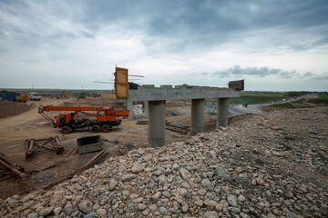 Fototapeta premium South Kazakhstan - April, 26 2012: Development of West Europe-West China highway. Construction of bridge of road junction against grey storm clouds