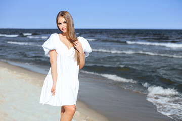 Happy, beautiful woman on the ocean beach standing in a white summer dress