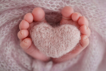Knitted pink heart in the legs of a baby. Soft feet of a new born in a pink wool blanket. Close-up...