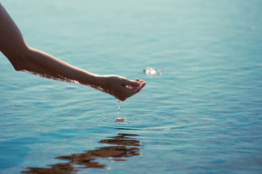 Hand scooping up water in calm lake surface 