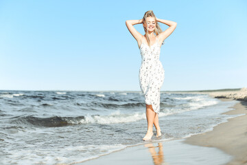 Happy blonde beautiful woman having fun on ocean beach while dancing in waves