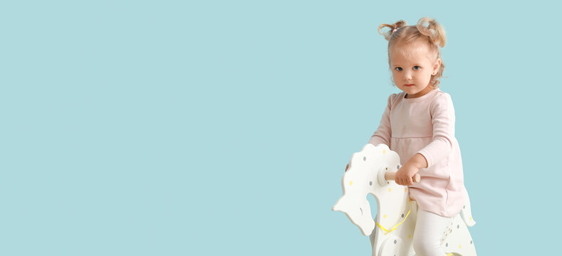 Adorable baby girl with rocking horse on light blue background with space for text