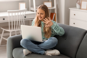 Little girl with laptop video chatting on sofa at home