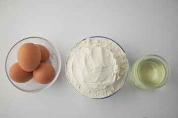 wheat flour in a bowl, eggs and oil on table 