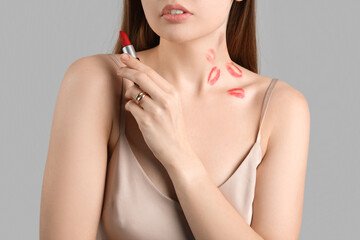 Young woman with lipstick marks and love bite on her neck against grey background, closeup