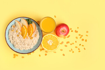 Bowl with tasty oatmeal, orange, apple and glass of juice on yellow background