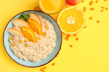 Bowl with tasty oatmeal, orange and apple slices on yellow background