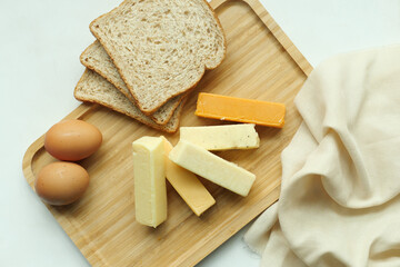 cheeses, egg and bread on wooden plate over table