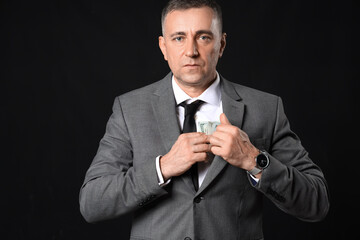 Mature businessman hiding bribe in jacket on dark background