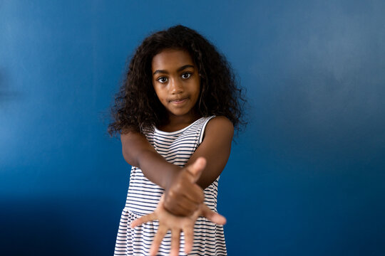 Portrait of biracial girl using sign language with hand on blue background - Powered by Adobe