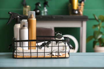 Basket with sprays, towel, scissors and hair clipper on table in beauty salon