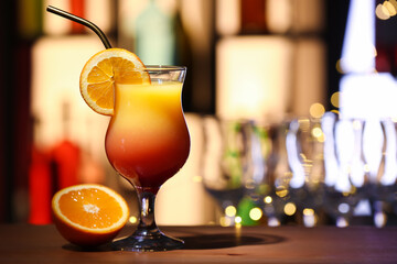Glass of tasty Tequila Sunrise and ripe orange on table in bar