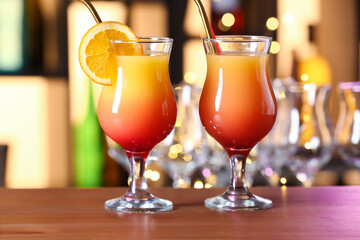 Glasses of delicious Tequila Sunrise on wooden table in bar