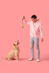 Young man playing with cute Labrador dog on pink background