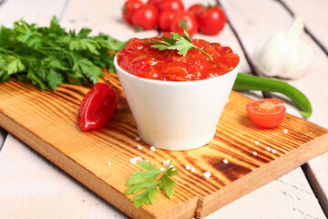 Board with bowl of delicious salsa sauce and ingredients on white wooden table