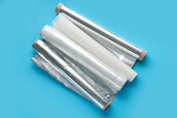 Rolls of aluminium foil, food film and baking paper on color background
