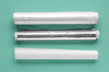 Rolls of baking paper, aluminium foil and food film on color background