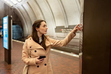 Washington DC Metro station, a young woman looking at a wall map for directions, holding a cellphone.