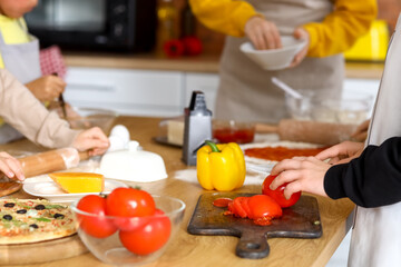 Little boy cutting tomato during cooking class in kitchen, closeup