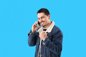 Happy young man talking by smartphone on light blue background