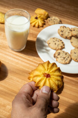 person's hand holding a sweet cookie to eat, table served with food and drink in studio, pastry shop with delicacies, wallpaper