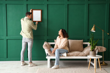 Young couple hanging blank frame on green wall at home